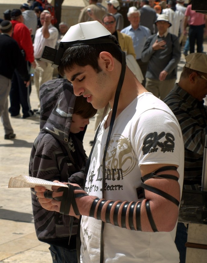 上图:一个犹太年轻人在前额和左臂上佩带经文匣(Tefillin),在耶路撒冷哭墙祷告。