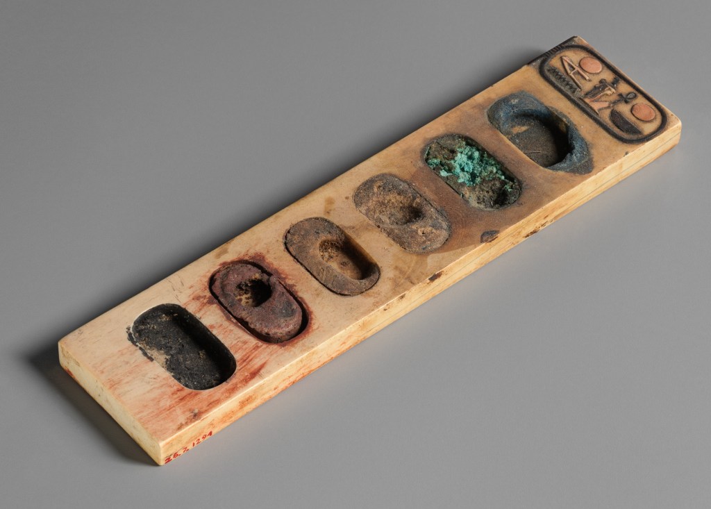 上图:主前1390-1352年的埃及调色板。这个调色板用一块象牙雕刻而成,有六个椭圆孔盛颜料,包括蓝色、绿色、棕色 、黄色、红色和黑色。一端的椭圆象形茧纹章(Cartouche)刻有法老阿蒙霍特普三世(Amenhotep III)的名字。古代文士所携带的墨盒就是一种调色板,板上有放笔的空档和装墨的凹陷处。笔用灯心草或苇杆削尖制成,墨用碳和树胶调和制作。红墨则加上氧化铁制成,用来书写标题或绘制书卷上的线条。此外,写字工具还包括削笔的刀子(耶三十六23)。