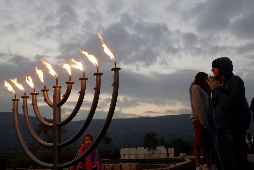 上图：光明节灯台（Hanukkah menorah）。主前168年，安提阿四世强制推行希腊化，在圣殿里竖起宙斯祭坛，用猪献祭，并强迫犹太人吃猪肉，导致了马加比起义。犹大马加比收复耶路撒冷以后，下令洁净圣殿，庆祝八天「修殿节」。当时人们在圣殿里只找到一罐有大祭司封印的用于点燃金灯台的灯油，无论是制作还是去外地取来这种专门洁净过的灯油，都需要八天时间。但这罐只能燃用一天的灯油，竟然一直燃烧了八天。为纪念此事，修殿节最主要的仪式是点燃九枝灯台，中间的灯盏用来点燃其它八支灯盏，每天多点一枝，一直到第八天，所以「修殿节」也被称为「光明节」。